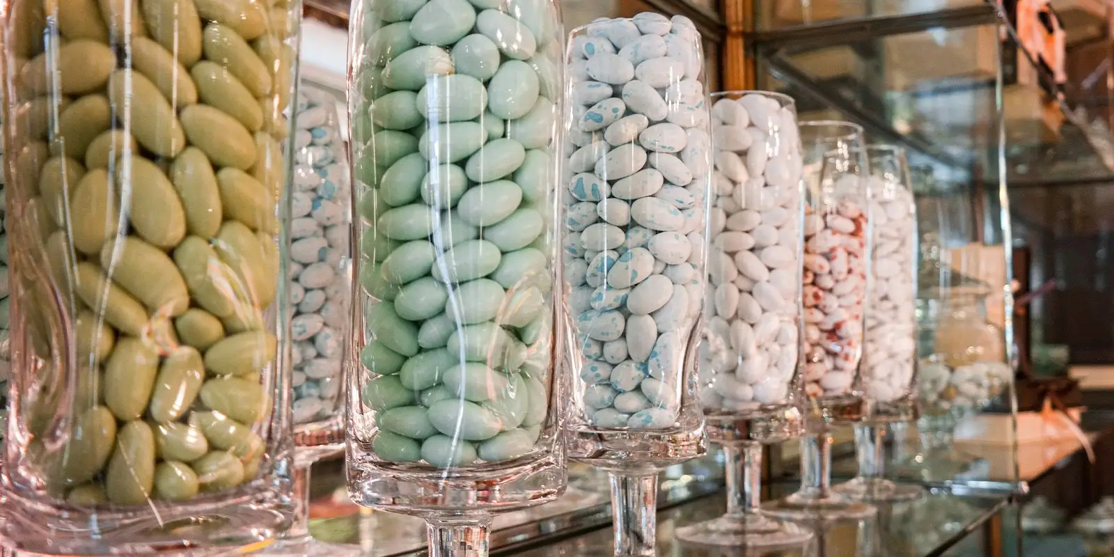 Le vetrine dei confetti: calici di vetro pieni di confetti verdi, azzurri, bianchi e rosa