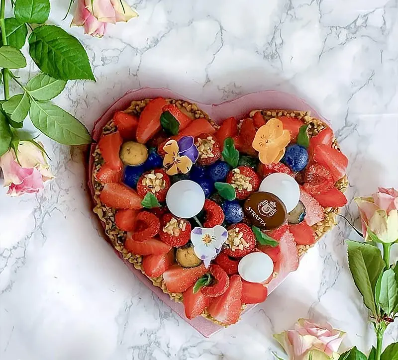 Una crostata a cuore con fragole, mirtilli e cioccolatini, fra le rose